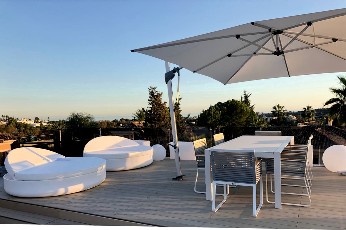 Large cantilever umbrella over a dining terrace at dusk with the sea on the horizon